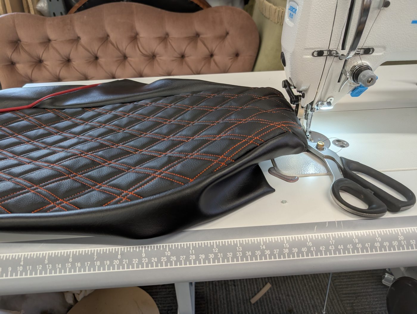 Sewing the cover on the industrial flat-bed — diamond-stitched top panel, plain sides, red piping caught in the seam.