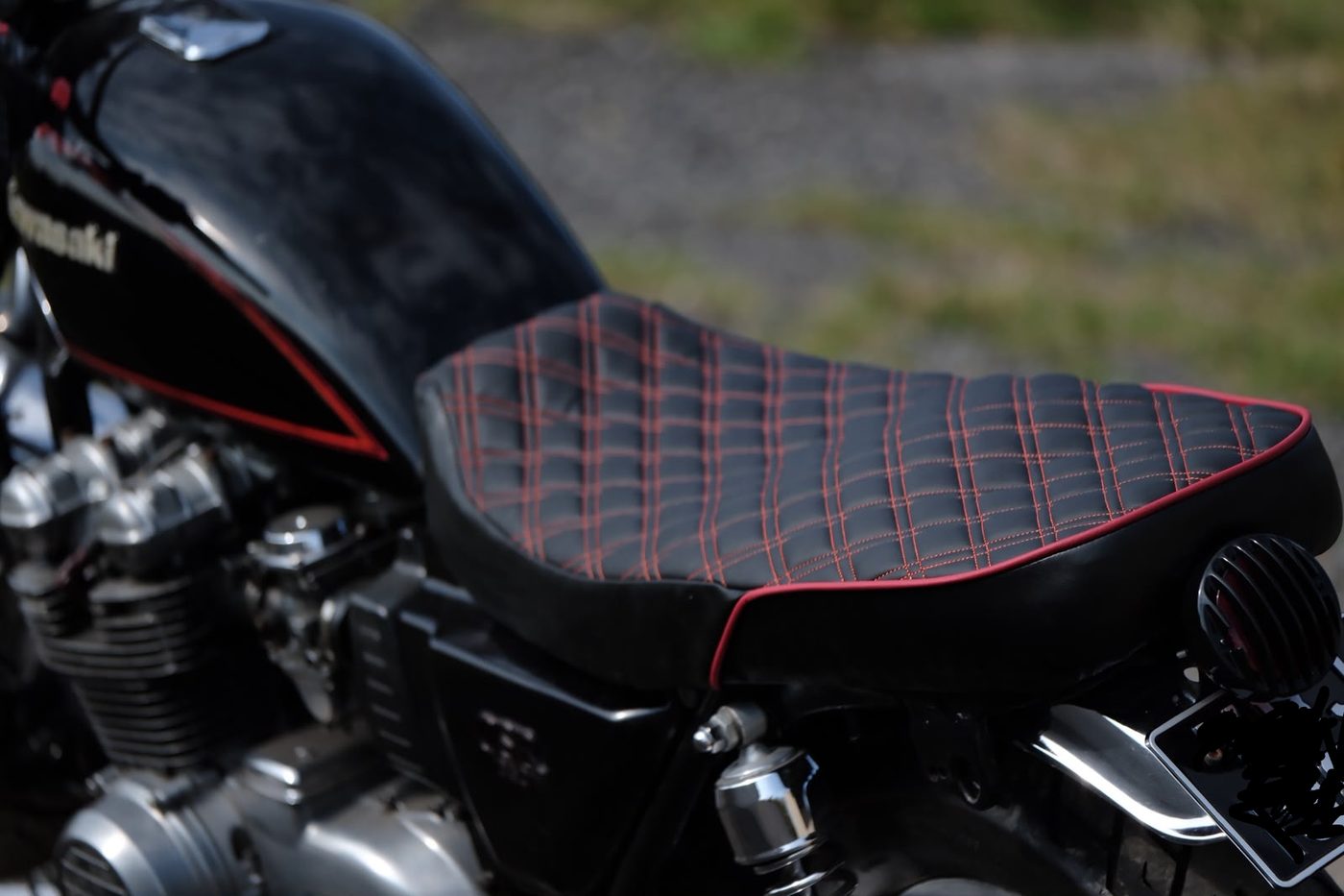 The detail that makes it — double-diamond stitching and red piping picking up the tank's pinstripe.