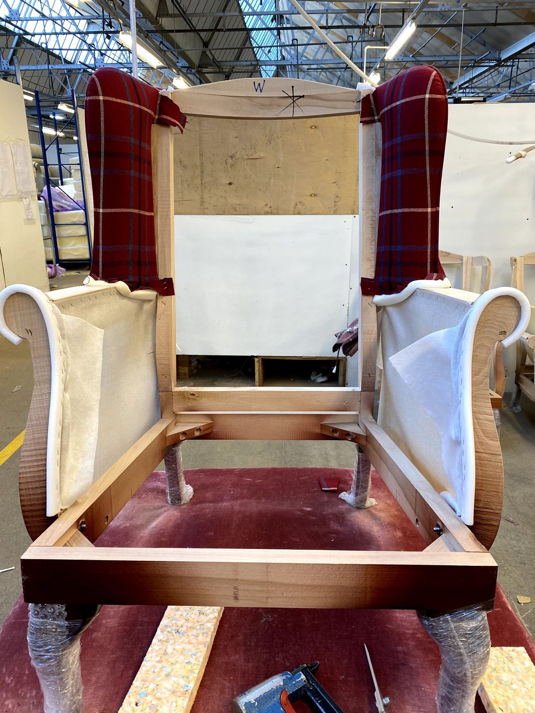 The prepared frame with the wings upholstered first — the check centred, the arms still in their under-wrap, the inside back and seat still to come.